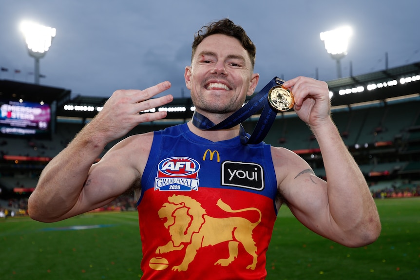 A footballer holds up a medal and smiles for the camera.
